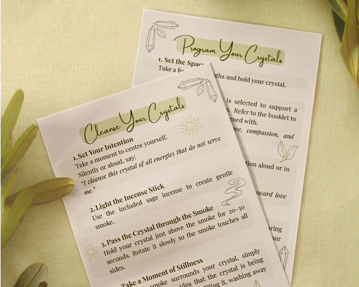 Two A6 crystal cards displayed on a light yellow background with natural greenery — showing front card ‘How to Cleanse Crystals’ and back card ‘How to Program Crystals’ — guides for cleansing, charging, and setting intentions with your crystals.