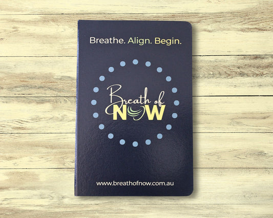 Front cover of dark blue meditation journal on light wooden floorboards — features text ‘Breath. Align. Begin.’, the Breath of NOW logo surrounded by a dotted circle, and the website ‘www.breathofnow.com.au’
 — designed for mindfulness, reflection, and intention setting.