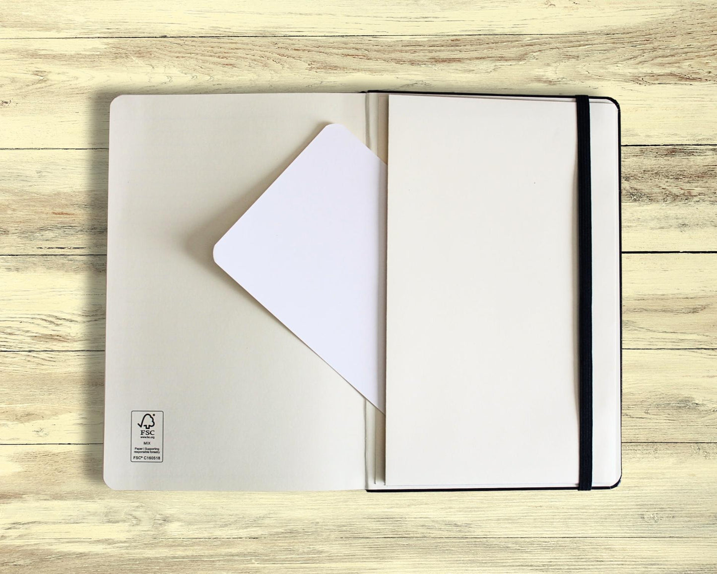 Open meditation journal showing the expandable accordion pocket on the last page with a blank A6 card half inserted — displayed on light wooden floorboards, designed for mindfulness and journaling reflections.